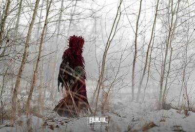 A cloaked woman walks in the foggy snow covered woods
