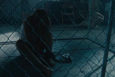 A woman sits in cage, silhouetted by the moon light.