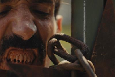 A man with vicious teeth stands by a locked fence