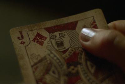 A playing card with a scary face being held in a woman's hand